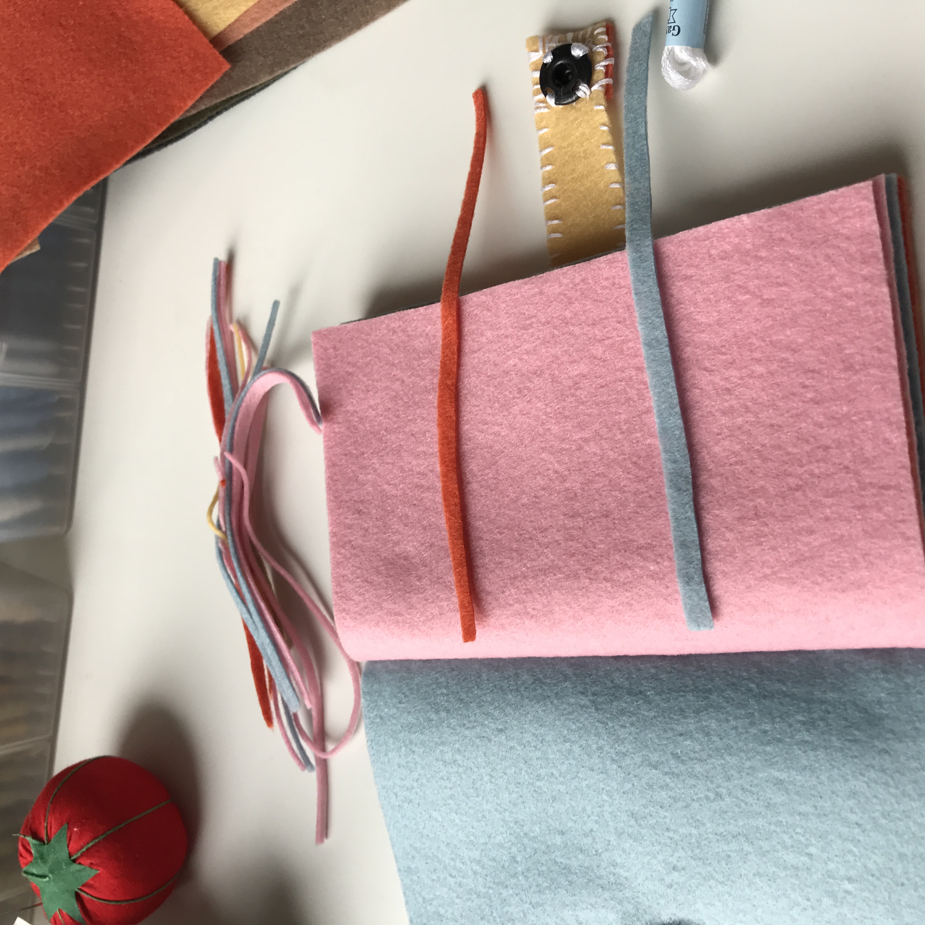 Close-up of a handmade felt notebook with pink and blue pages, a red ribbon closure and colorful tassels.