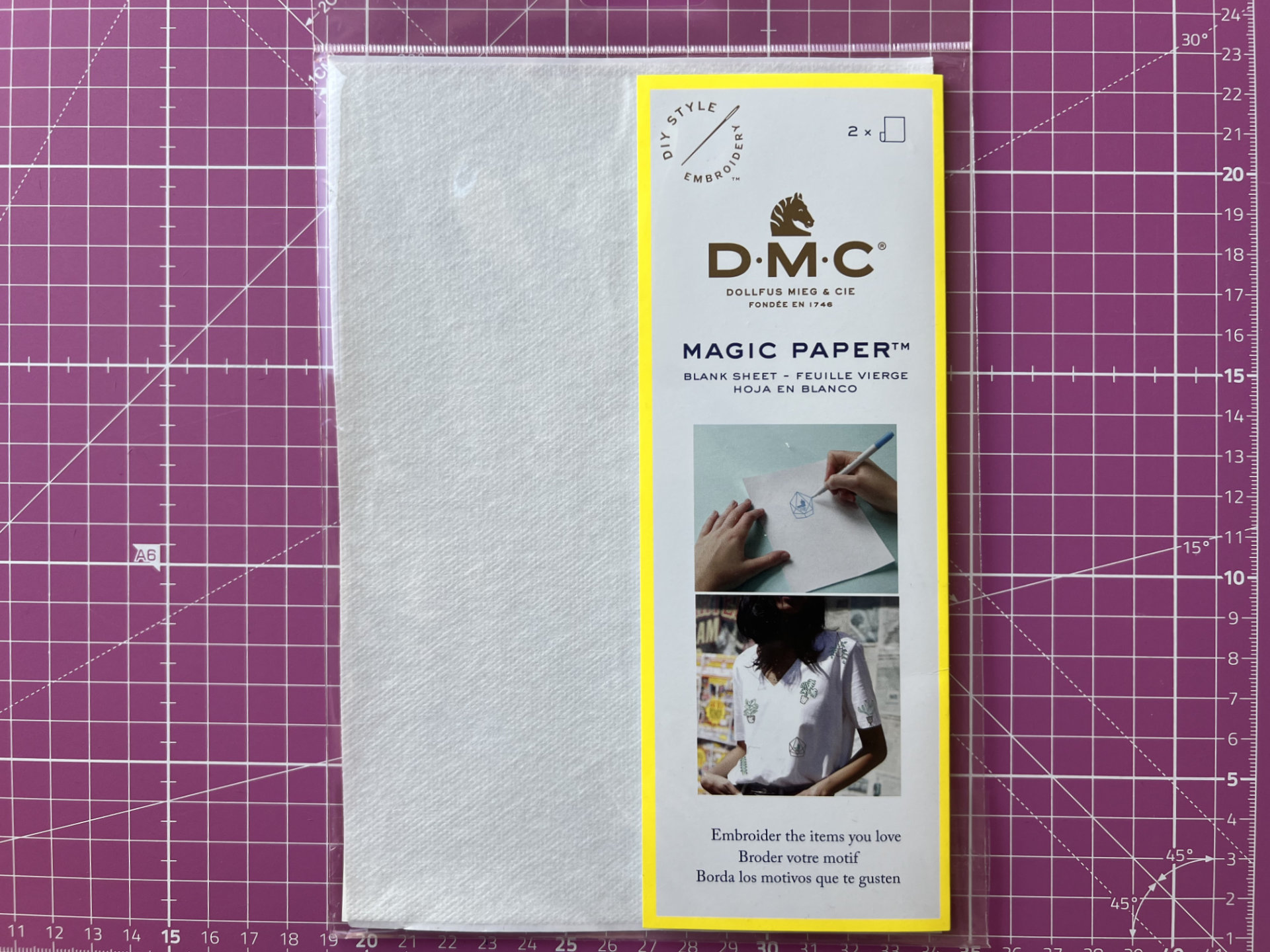 DMC Magic Paper packaging on a purple grid cutting mat with a bright yellow border and demo photos.