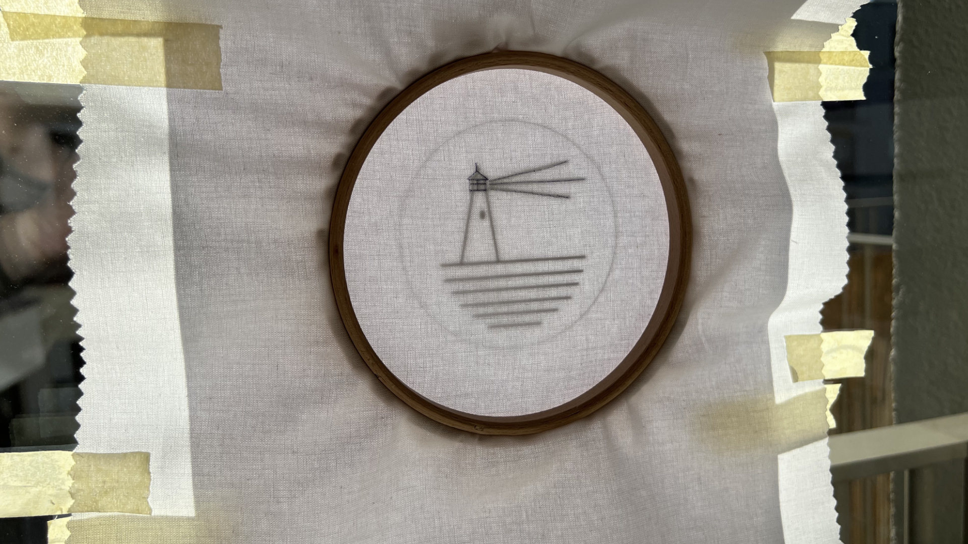 Embroidery hoop with a simple lighthouse sketch and water lines on pale linen fabric.
