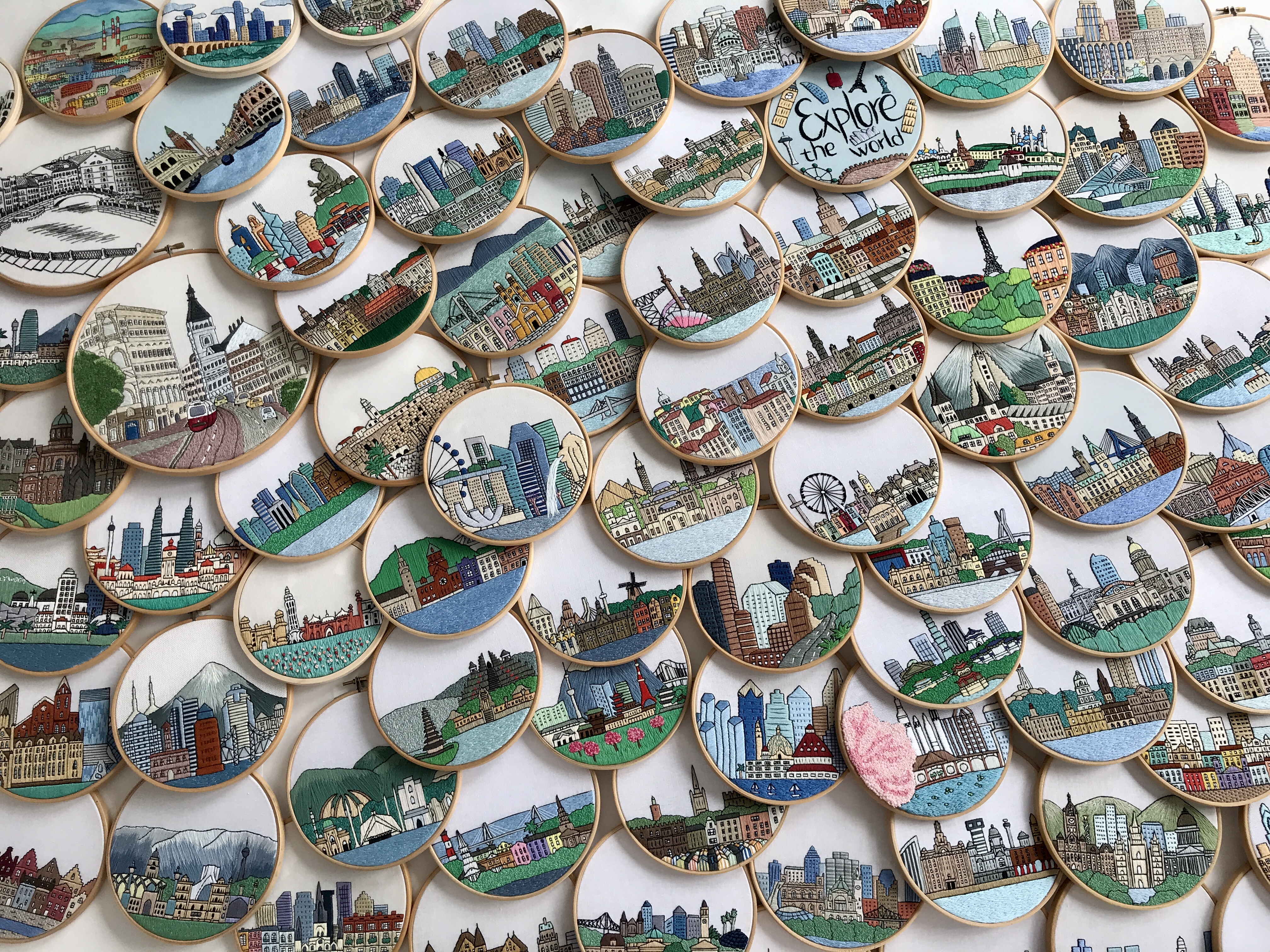 Array of round embroidered hoops with colorful city skylines stacked together. Made by @faimyxstitch