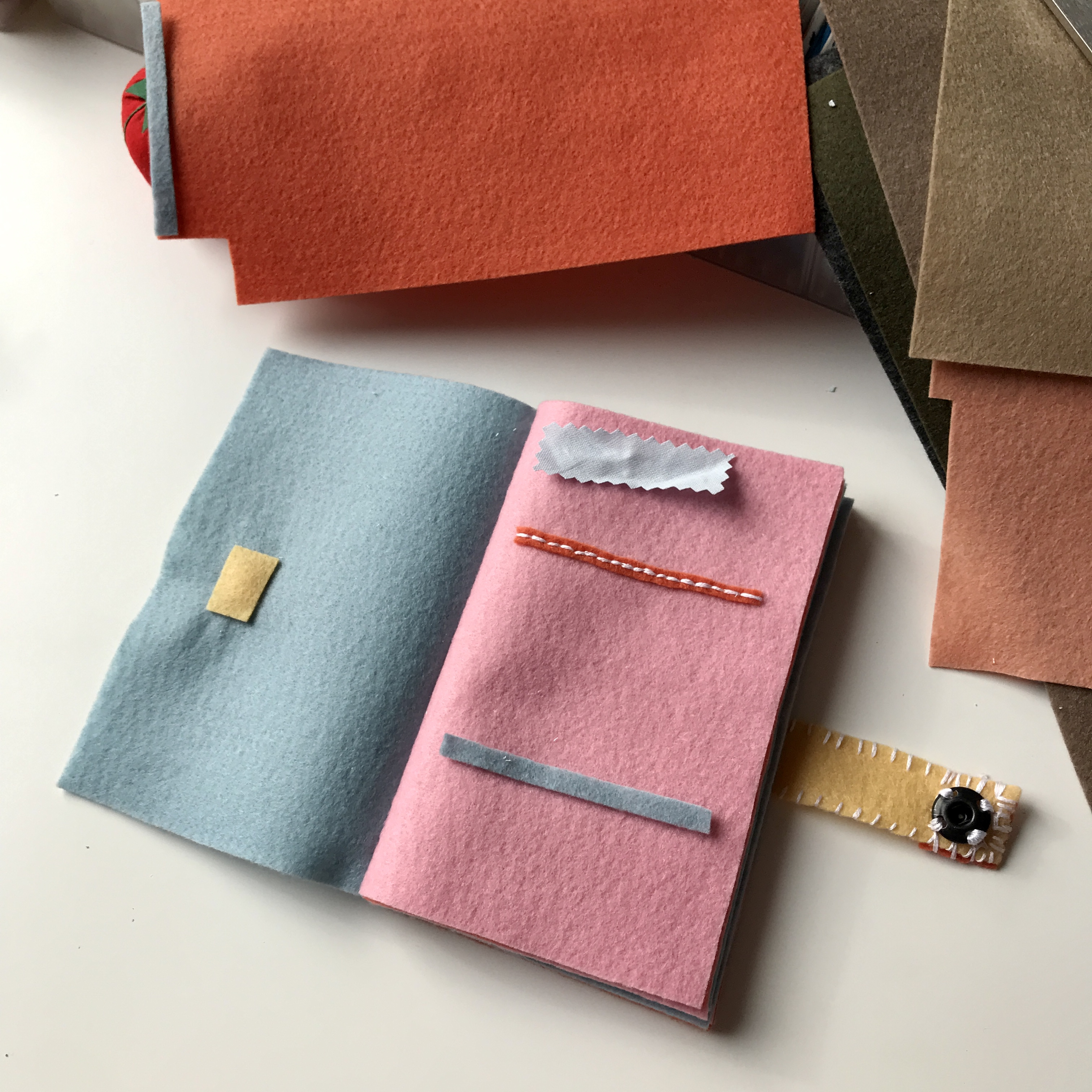 Handmade felt notebook with blue and pink pages, stitched accents and fabric swatches on a craft desk