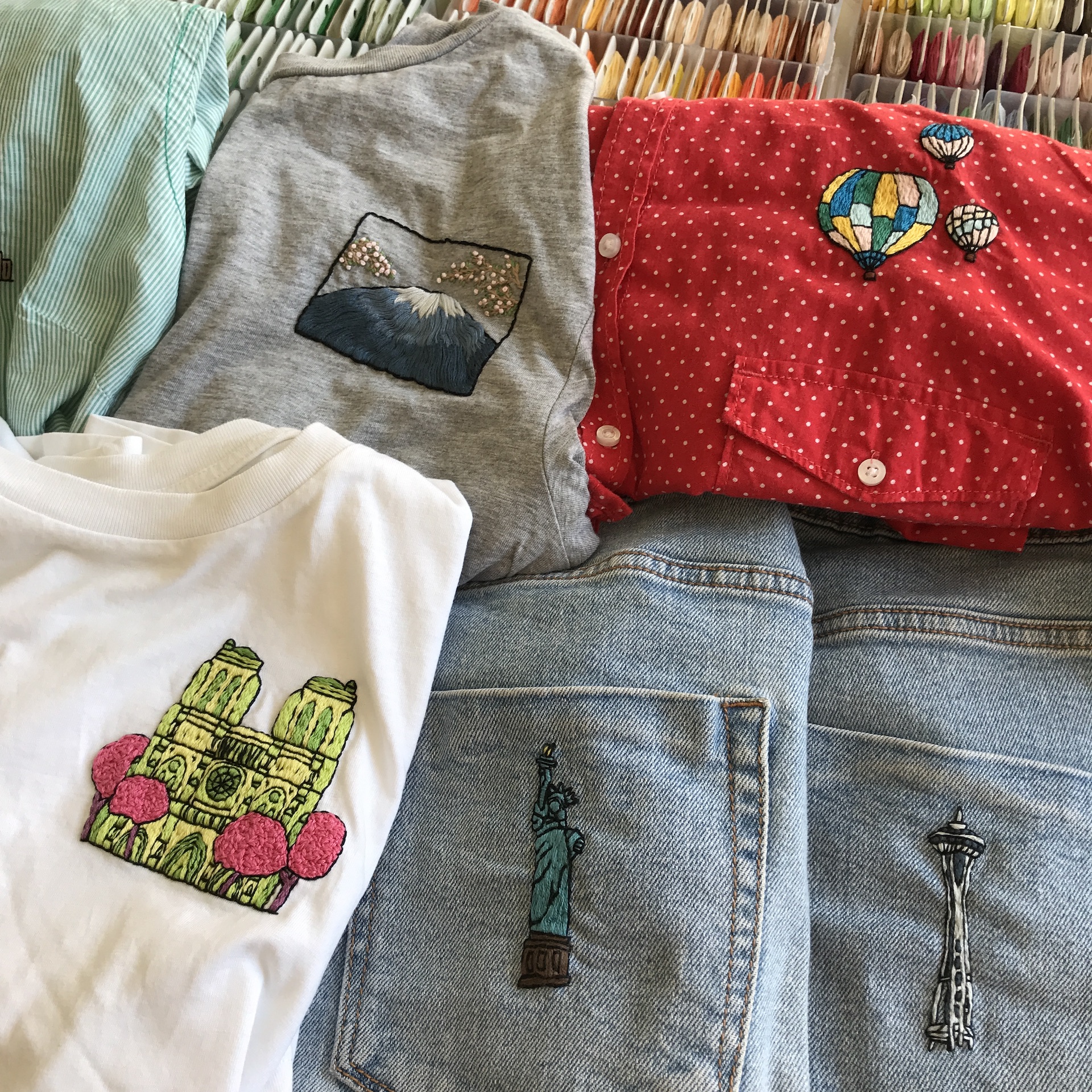 Assorted embroidered patches on shirts and denim, featuring mountains, balloons, and city landmarks.