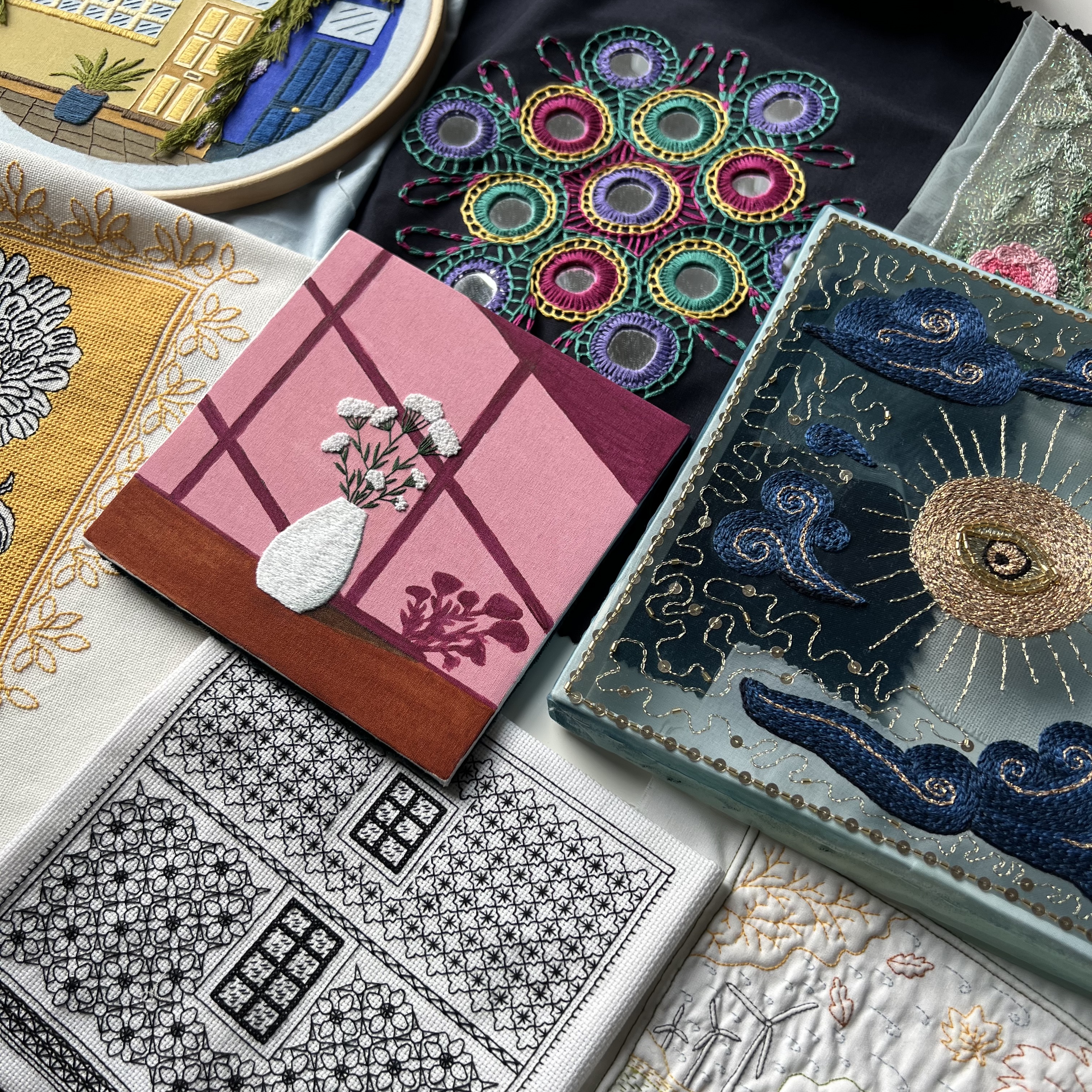 Assorted hand-embroidered textiles with colorful patterns, vases, sun motifs, and decorative embroidery.