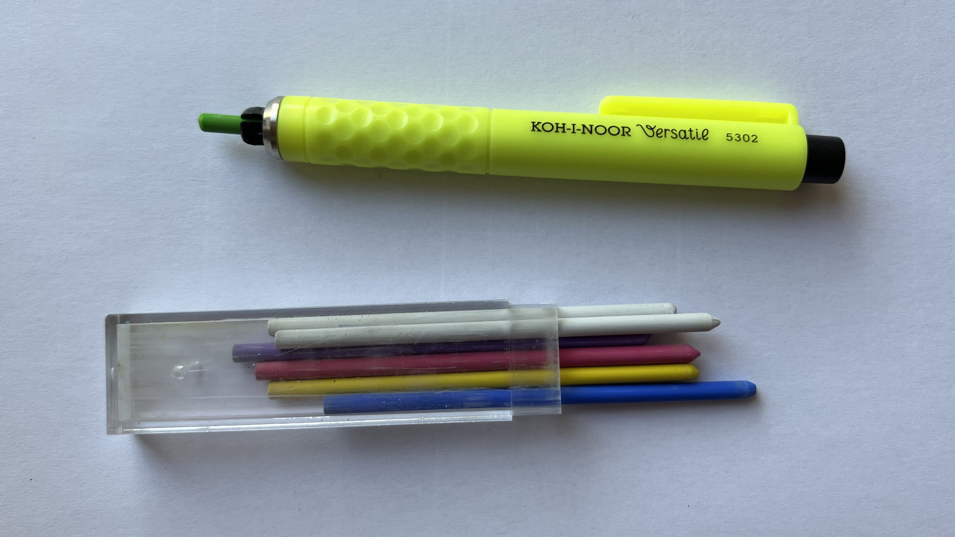 Neon yellow Koh-I-Noor Versatile chalk pen with textured grip beside a plastic case of colored leads.