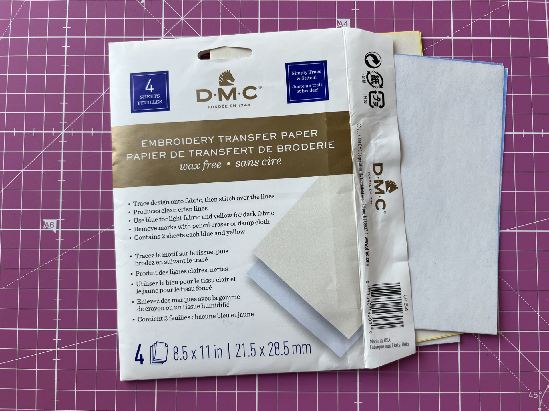DMC embroidery transfer paper pack with four sheets on a pink grid cutting mat.