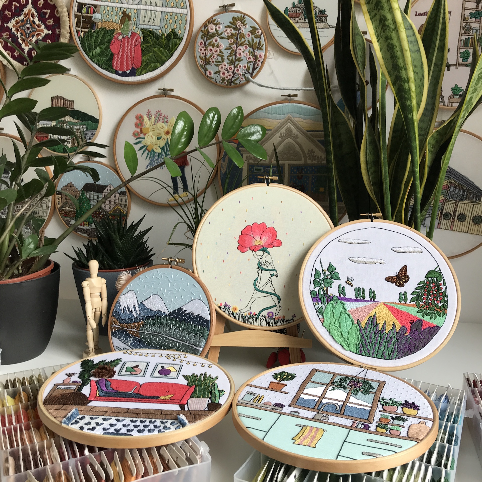 Assorted embroidery hoops with colorful stitched designs—landscapes, florals, and cozy interiors.