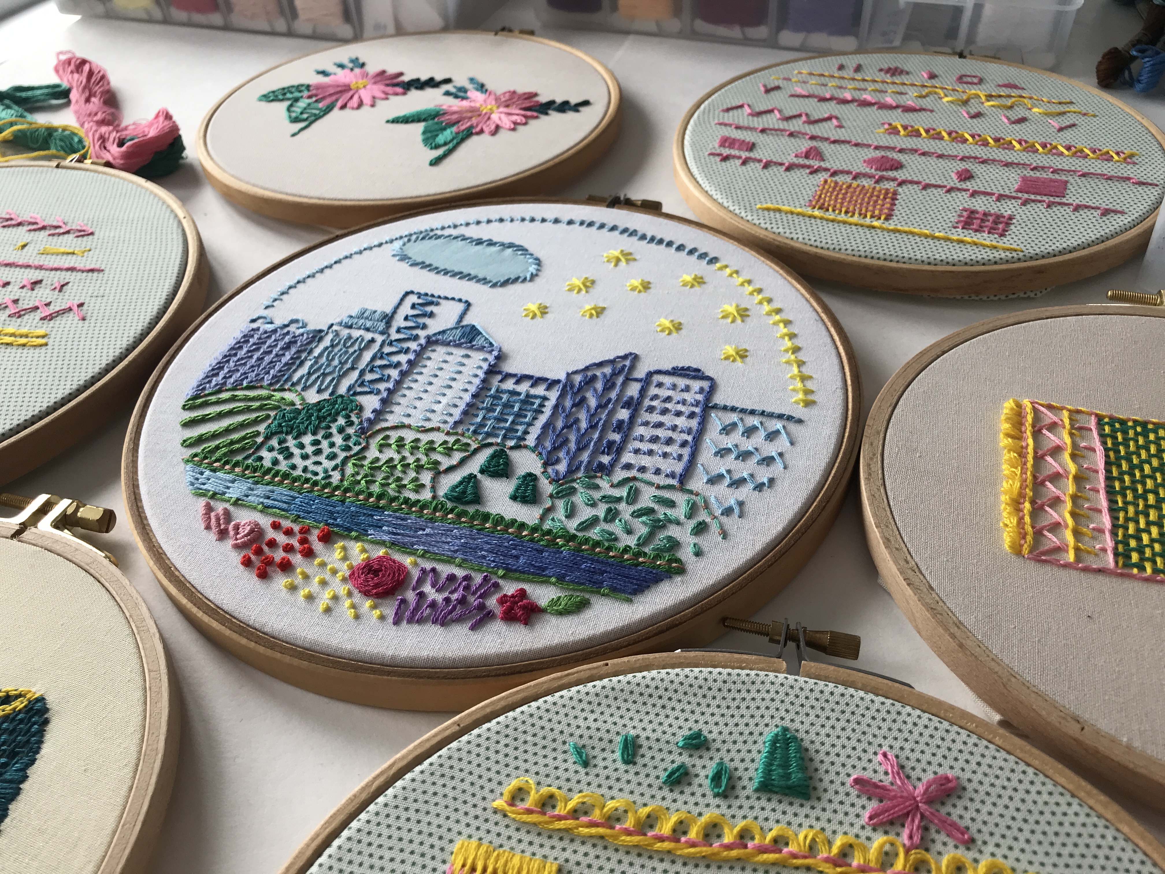 Colorful cityscape embroidery in a hoop with buildings, river, and stars. Embroideries from online course Hand embroidery stitches and practice by @faimyxstitch