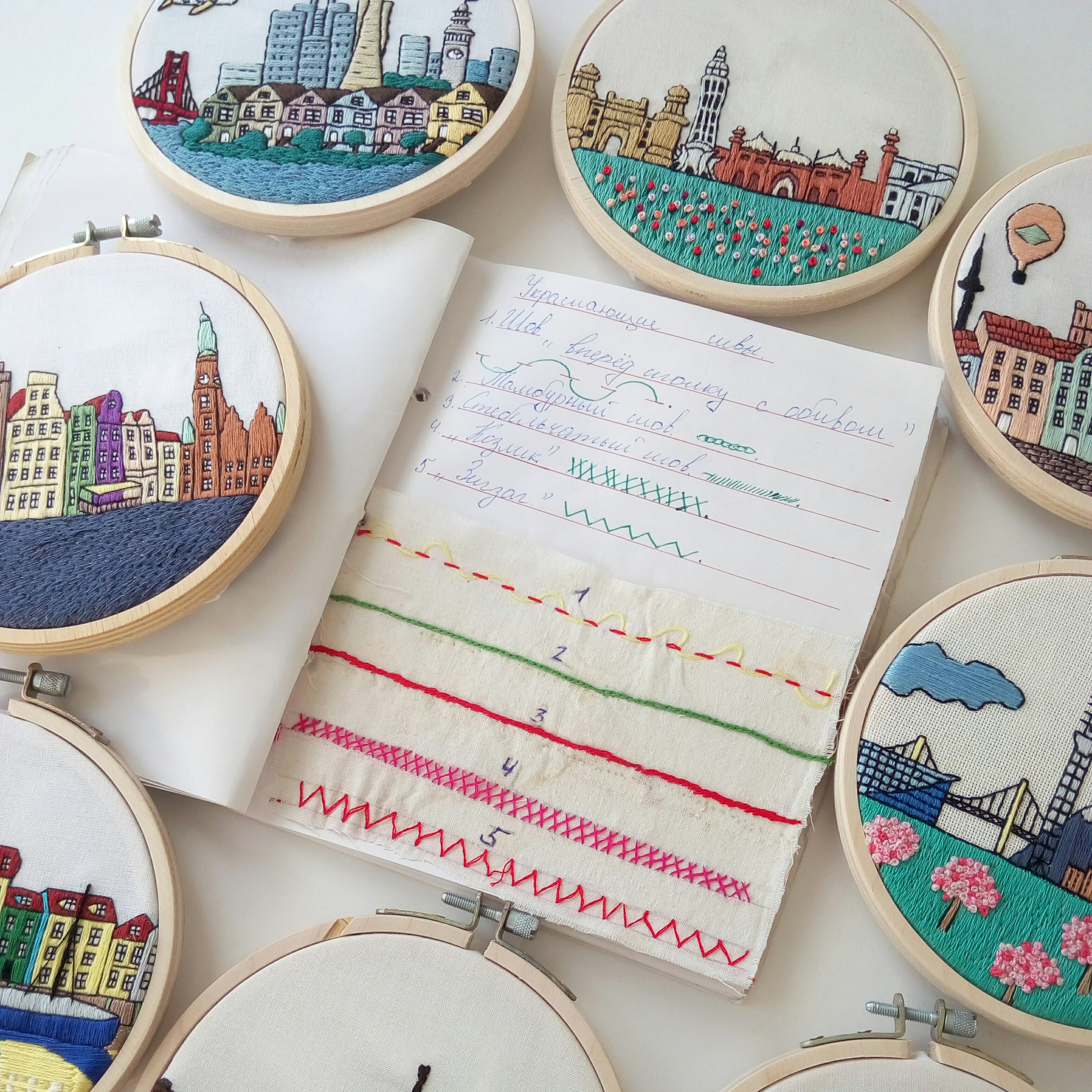 Set of embroidery hoops with colorful city skylines and a fabric swatch on a notebook