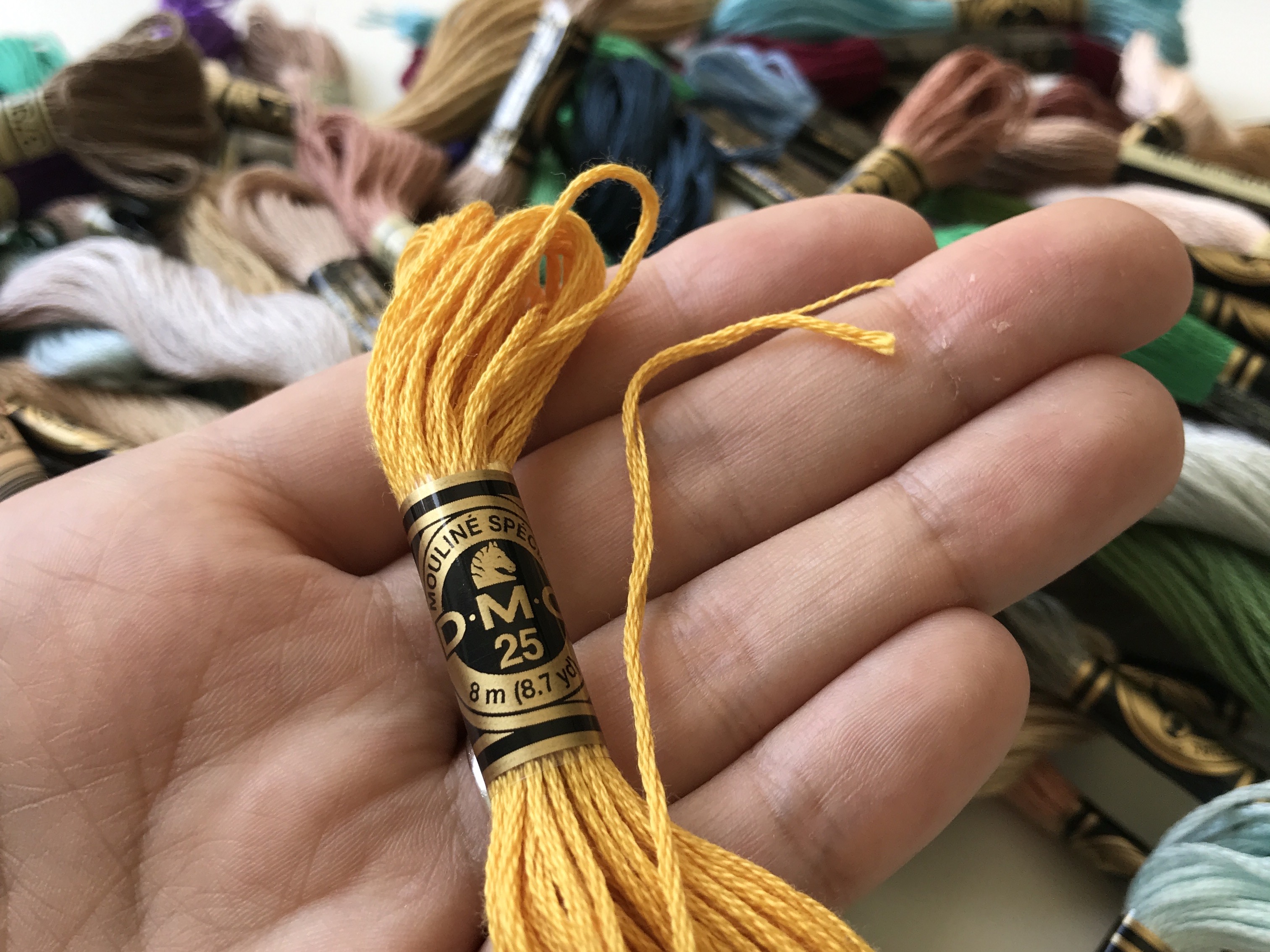 Bright yellow embroidery floss skein held in hand with assorted threads in the background