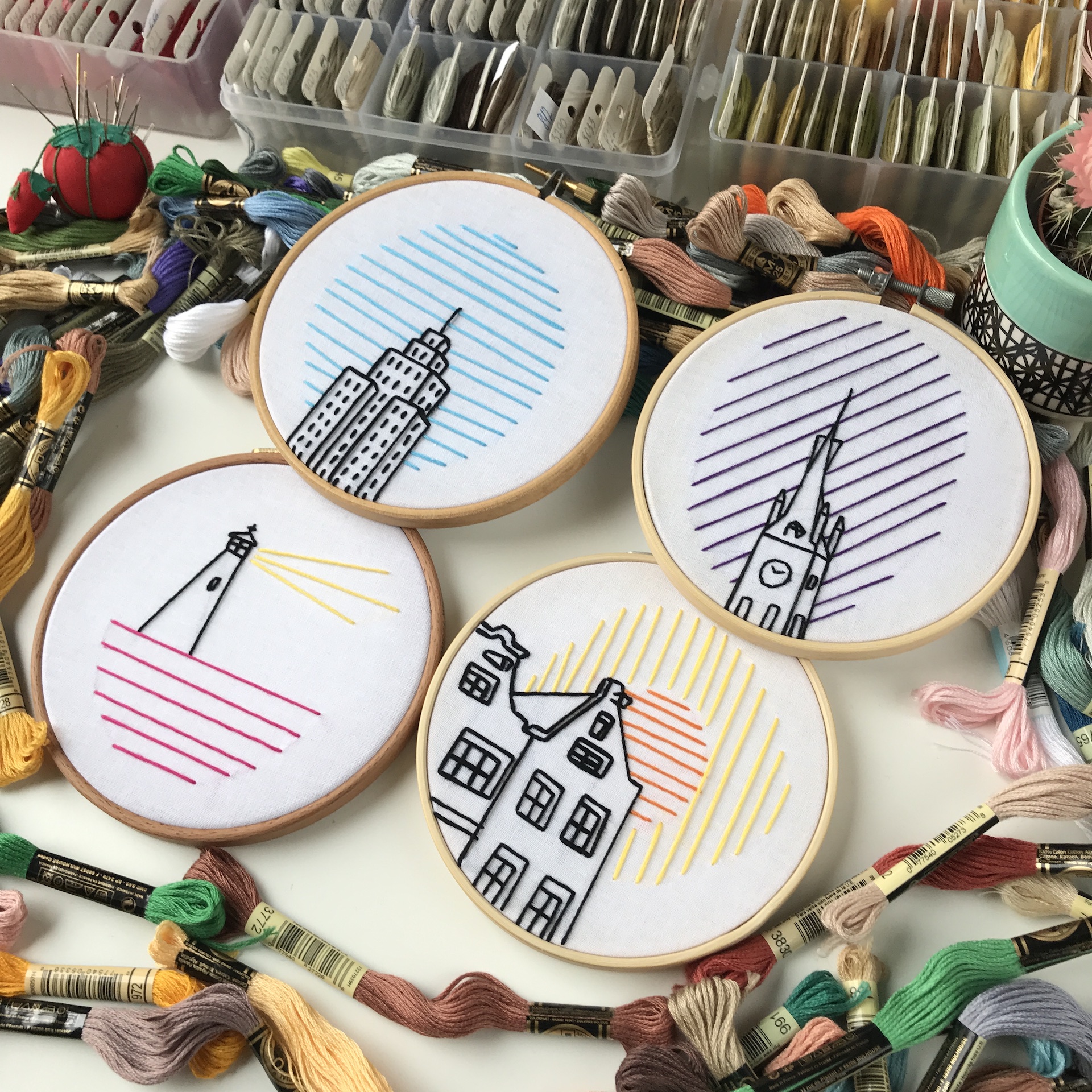 Five embroidery hoops with minimalist city skylines against colorful striped backgrounds