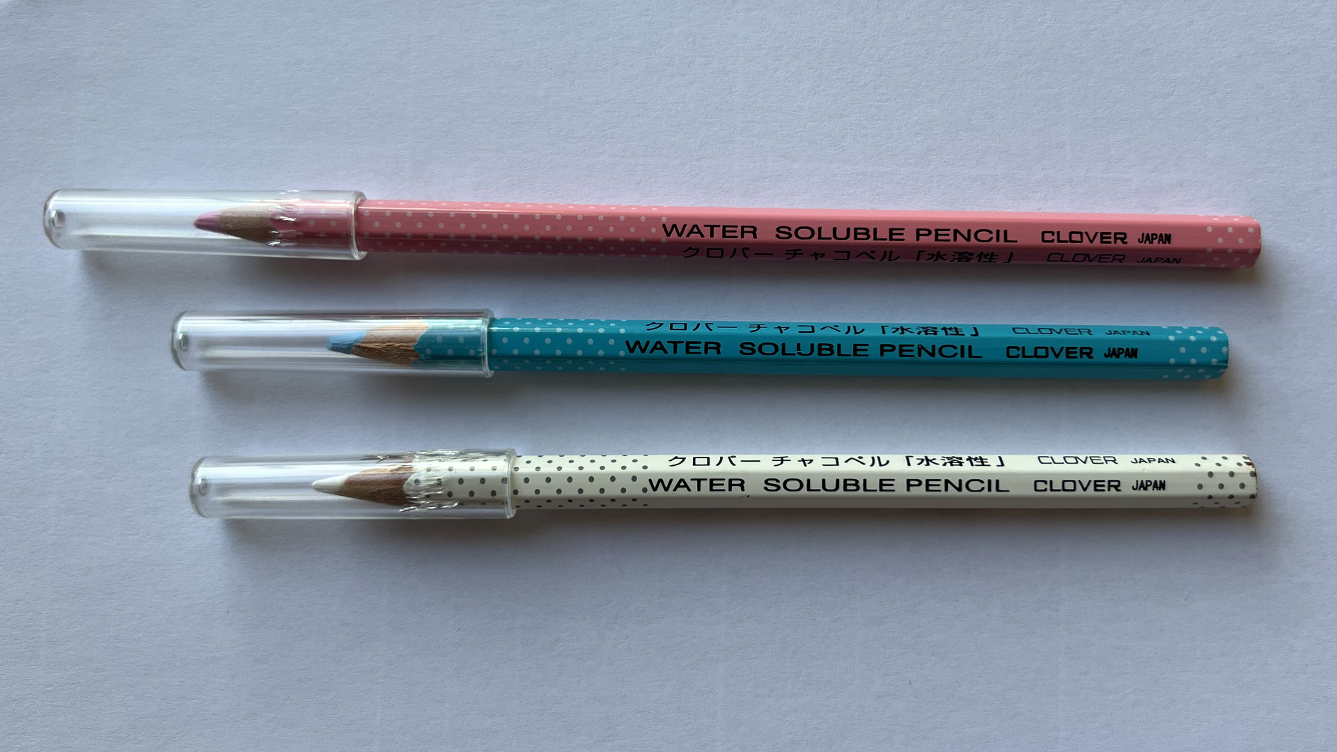 Three Clover water-soluble pencils in pink, turquoise, and white with polka dots and clear caps.